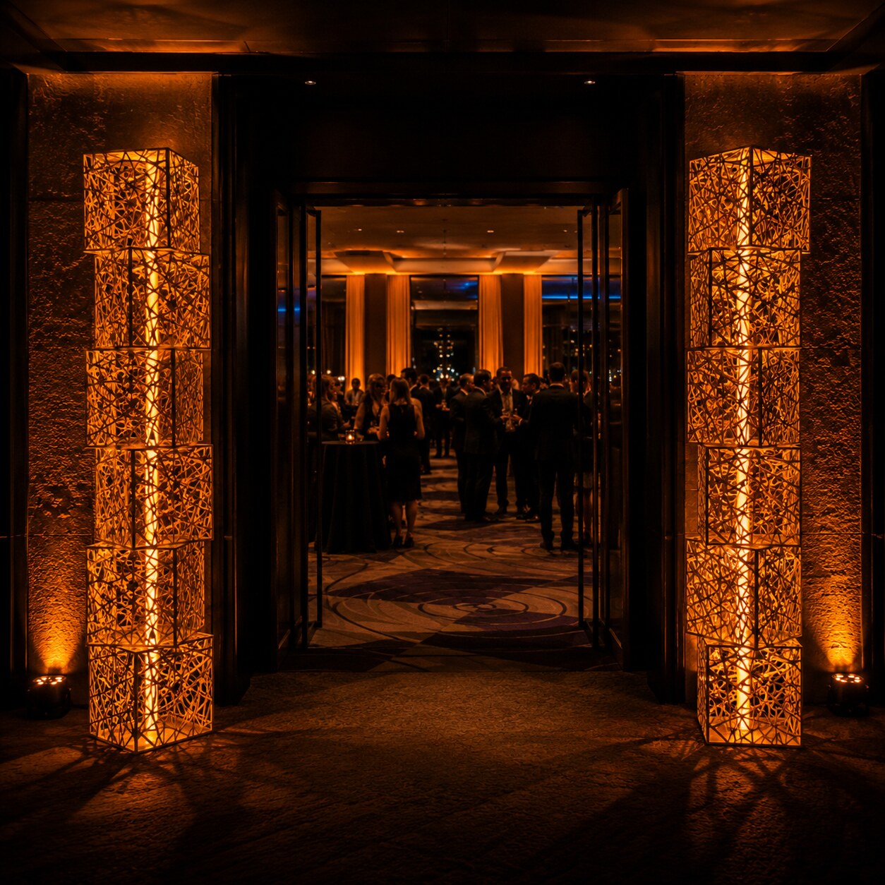 Illuminated orange woven-lattice entrance pillars flanking a venue doorway